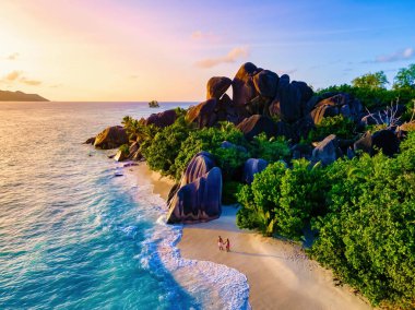 Anse Source d 'Argent plajı, La Digue Adası, Seyshelles, La Digue Seychelles kuş bakışı hava aracı manzaralı tropikal adayı, günbatımında sahilde yürüyen iki erkek ve kadın.