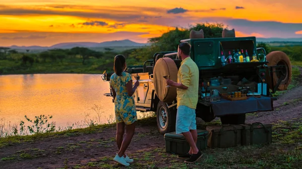 A couple of men and an Asian woman on safari in South Africa, a luxury safari car during a game drive, couple men and woman on safari in South Africa at sunset sundowner with cocktails and drinks