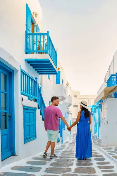 Romantic couple of men and women walking at the street of Mykonos Greek village in Greece during sunrise, colorful streets of Mikonos village