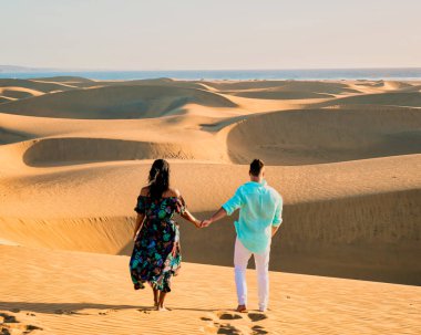 Maspalomas sahilinde yürüyen çift Gran Canaria İspanya, Maspalomas 'ın kum tepeleri çöllerinde erkek ve kadın sabah güneş doğarken İspanya Avrupa