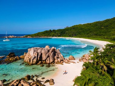Anse Cocos plajı, La Digue Adası, Seyşeller, La Digue Seyşeller 'in insansız hava görüntüsü tropik bir adanın kuş bakışı görüntüsü, günbatımında sahilde yürüyen birkaç erkek ve kadın lüks bir tatilde.
