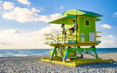 Miami Beach, Miami Florida sahilinde bir çift, Miami 'de cankurtaran kulübesi Asyalı kadınlar ve gün batımında sahilde beyaz erkekler. Erkek ve kadın güneşin doğuşunu izliyor.