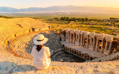 Hierapolis antik kenti Pamukkale Türkiye, Unesco Heritage harabelerinde gün batımını izleyen şapkalı genç bir kadın. Türkiye 'deki eski amfitiyatroda gün batımını izleyen Asyalı kadınlar