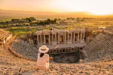 Hierapolis antik kenti Pamukkale Türkiye, Unesco Heritage harabelerinde gün batımını izleyen şapkalı genç bir kadın. Türkiye 'deki eski amfitiyatroda gün batımını izleyen Asyalı kadınlar