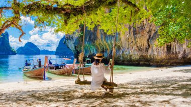 Tayland 'daki Koh Hong Adaları' nın Koh Loa Lading Krabi Tayland bölgesinde salıncakta sallanan kadınlar. Güneşli bir günde kireçtaşı kayalıkları ve uzun kuyruklu tekneleri olan güzel bir sahil.