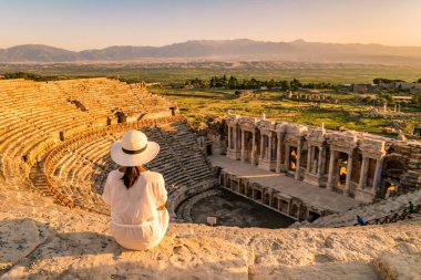 Hierapolis antik kenti Pamukkale Türkiye, Unesco Heritage harabelerinde gün batımını izleyen şapkalı genç bir kadın. Türkiye 'deki eski amfitiyatroda gün batımını izleyen Asyalı kadınlar