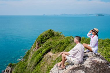 Bir çift Avrupalı erkek ve Asyalı kadın Ko Kham Adası Sattahip Chonburi Samaesan Tayland 'a tekne gezisine gittiler. Okyanus manzaralı bir kayanın üzerinde oturan bir çift.