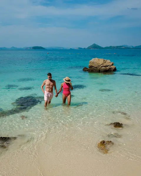 A couple of European men and Asian woman on a boat trip at Ko Kham Island Sattahip Chonburi Samaesan Thailand, a couple at a tropical island with turqouse colored ocen relaxing on the beach