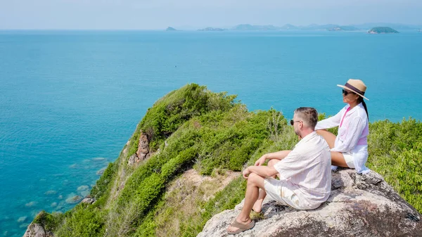 A couple of European men and an Asian woman on a boat trip at Ko Kham Island Sattahip Chonburi Samaesan Thailand, a couple sitting on a rock with a view over the ocean at a viewpoint