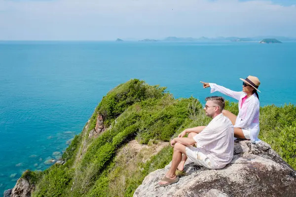 A couple of European men and an Asian woman on a boat trip at Ko Kham Island Sattahip Chonburi Samaesan Thailand, a couple sitting on a rock with a view over the ocean at a viewpoint