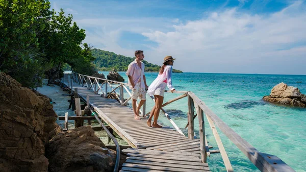 A couple of European men and an Asian woman on a boat trip at Ko Kham Island Chonburi Samaesan Thailand, a couple walking at a wooden bridge jetty on a tropical island with turqouse colored ocen
