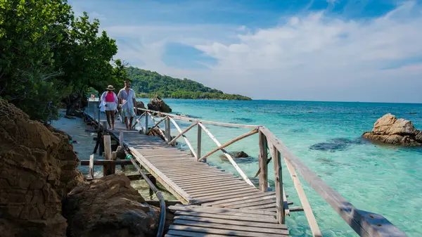 Bir çift Avrupalı erkek ve Asyalı bir kadın Ko Kham Adası Sattahip Chonburi Samaesan Tayland 'a tekne gezisine gittiler. Tropik bir adada turkuvaz renkli oktanlı ahşap iskelede bir çift.