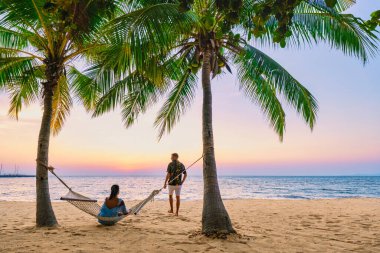 Najomtien Sahili Pattaya Tayland, palmiye ağaçlı tropik bir sahilde gün batımı. Bir çift adam ve orta yaşlı bir kadın Na Jomtien 'de palmiye ağaçlarıyla plajda gün batımını izliyorlar.