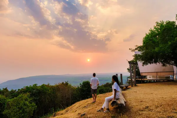 men and women watching the sunset at a mountain camping in Phitsanulok Thailand. luxury glamping in the nature of Northern Thailand at sunset looking out over the mountains