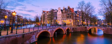 Günbatımında Amsterdam Kanalı, Hollanda 'da geceleri eski tarihi evlerle Amsterdam Kanalı köprüsü. Tarihsel eski Amsterdam kasabasında panoramik manzara