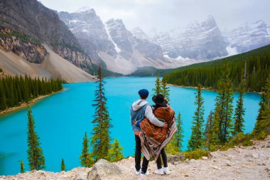 Kanada 'da soğuk bir kar gününde Moraine Gölü, Moraine Gölü' nün turkuaz suları Banff Ulusal Parkı Kanada Kayalıkları 'nda karla kaplı. Kanada 'da bir gölün kenarında duran genç çift.