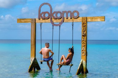 Curacao Karayip Adası 'ndaki Kokomo Sahili' nde salıncakta sallanan bir çift Karayip adası Curacao 'da tatil sırasında turkuaz renkli okyanusta dinlenen erkek ve kadın.
