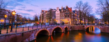 Günbatımında Amsterdam Kanalı, Hollanda 'da geceleri eski tarihi evlerle Amsterdam Kanalı köprüsü. Tarihsel eski Amsterdam kasabasında panoramik manzara