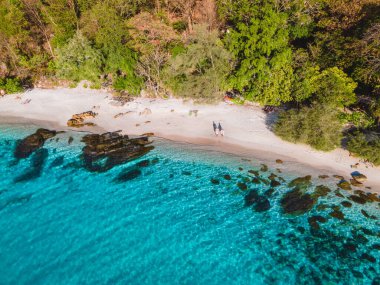 Koh Samet Adası Tayland, Tayland 'ın Samed Adası sahilinde iki erkek ve kadının üzerinde havadan insansız hava aracı görüntüsü. Turkuaz renkli bir okyanus ve beyaz bir tropik plaj.