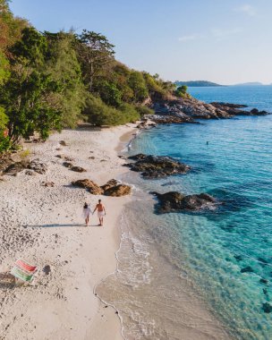 Koh Samet Adası Tayland, Tayland 'ın Samed Adası sahilinde turkuaz renkli bir okyanus ve beyaz tropikal bir plajla yürüyen bir çift erkek ve kadının yukarıdan insansız hava aracı görüntüsü.