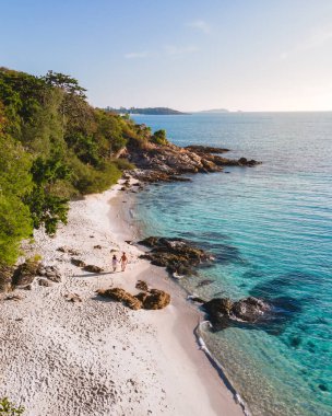 Koh Samet Adası Tayland, Tayland 'ın Samed Adası sahilinde iki erkek ve kadının üzerinde havadan insansız hava aracı görüntüsü. Turkuaz renkli bir okyanus ve beyaz bir tropik plaj.