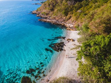 Koh Samet Adası Tayland, Tayland 'ın Samed Adası sahilinde iki erkek ve kadının üzerinde havadan insansız hava aracı görüntüsü. Turkuaz renkli bir okyanus ve beyaz bir tropik plaj.