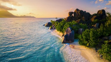 Anse Kaynağı dArgent La Digue Seyşeller, birkaç beyaz erkek ve Asyalı kadın, Anse Source dArgent La Digue Seychelles 'de lüks bir tatil sırasında tropikal bir plajda