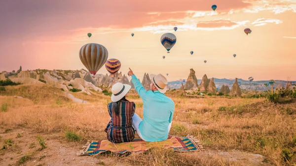 Cappadocia Turkey during sunrise, a couple mid age men and women on vacation in the hills of Goreme Cappadocia Turkey, men and woman looking sunrise with hot air balloons in Cappadocia Turkey holiday