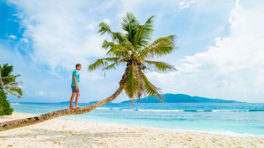 Young men relaxing at a palm tree on a tropical white beach at the La Digue Seychelles Islands.
