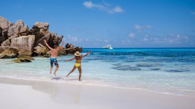 Anse Cocos Sahili La Digue Adası Seyşelleri, Seyşeller 'de lüks bir tatilde sahilde yürüyen mutlu bir çift erkek ve kadın, tatilde mutlu bir şekilde gökyüzüne atlayan erkekler ve kadınlar. 