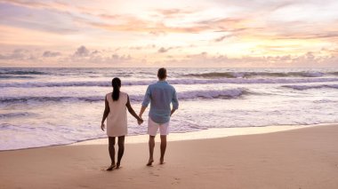 Phuket Tayland 'da tropik bir plajda gün batımını izleyen bir çift kadın ve erkek.