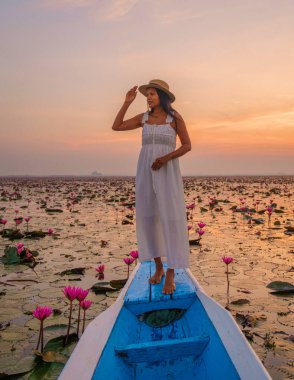 Kızıl Lotus Denizi 'nde gün doğumu, Nong Harn Gölü, Udon Thani, Tayland. Isaan 'daki Red Lotus Gölü' nde bir teknede şapkalı ve elbiseli Asyalı bir kadın.