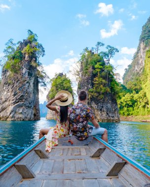 Khao Sok Tayland 'da uzun kuyruklu bir teknenin önünde birkaç kadın ve erkek Khao Sok Ulusal Parkı' ndaki Khao Ulusal Parkı 'ndaki göl manzaralı dağlarda, erkek ve kadın tekne gezisinde.