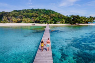 Koh Kham Trat Tayland okyanusunda tahta bir iskelede yürüyen çift, Koh Mak Tayland yakınlarındaki tropik adanın havadan görünüşü. Palmiye ağaçları ve büyük siyah kaya taşlarıyla beyaz kumlu sahil 