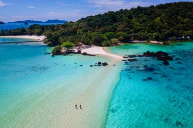 Koh Mak Tayland yakınlarındaki Koh Kham Trat Tayland plajında yürüyen çift. Beyaz kumlu sahil, palmiye ağaçları ve okyanusta büyük siyah kaya taşları.