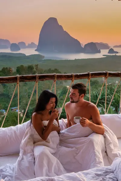 A couple in an outdoor bedroom watching the sunrise over Sametnangshe mountains in Phangnga Bay with mangrove forest in the Andaman Sea Phangnga, Thailand