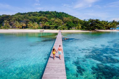Koh Mak Tayland yakınlarındaki Koh Kham Trat Tayland 'da tahta bir iskelede yürüyen çift. Palmiye ağaçlı beyaz kumlu sahil