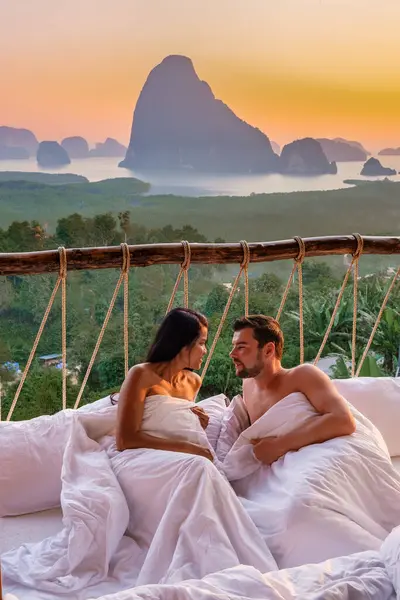 A couple in an outdoor bedroom watching the sunrise over Sametnangshe mountains in Phangnga Bay Thailand