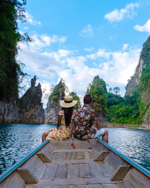 Khao Sok Tayland 'da uzun kuyruklu bir teknenin önünde birkaç kadın ve erkek güneşli bir günde Khao Sok Ulusal Parkı' ndaki gölde manzaralı dağlar.