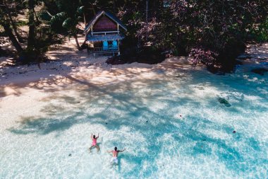 Koh Wai Adası Trat Tayland, Koh Chang yakınlarında teneke bir tropikal adadır. Kumsaldaki ahşap bambu kulübesi. Tayland 'da tropik bir adada okyanusta yüzen bir çift genç adam ve kadın.