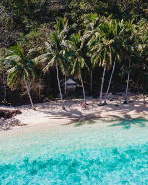 Sahilde palmiye ağaçları olan ahşap bambu kulübesi. Tayland, Koh Wai Adası 'ndaki tropikal bir adada bir çift genç adam ve kadın.