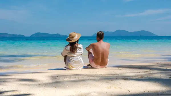 一对年轻夫妇在泰国度豪华假期时坐在热带海滩上 而这对年轻夫妇则躺在泰国高伟岛的海滩上 — 图库照片