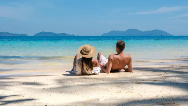 一对年轻夫妇在泰国度豪华假期时坐在热带海滩上 而这对年轻夫妇则躺在泰国高伟岛的海滩上 — 图库照片