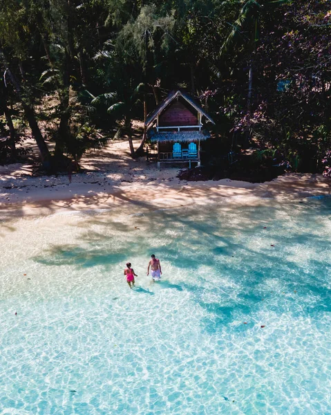 高伟岛是靠近高昌的一个微小的热带岛屿 海滩上的木制竹屋平房 一对年轻夫妇在泰国热带岛屿上的蓝色海洋中游泳 — 图库照片