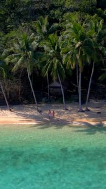 Koh Wai Adası Trat Tayland, Koh Chang yakınlarında. Kumsaldaki ahşap bambu kulübesi ve Tayland 'da tropik bir adada sahilde yürüyen genç bir çift kadın ve erkek.