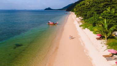 Koh Libong, Trang, Tayland, Andaman Denizi 'nde mavi gökyüzünde kristal berrak su bulunan güzel bir sahil manzarası. Güneşli bir akşamda kumsalda yürüyen bir çift kadın ve erkek.