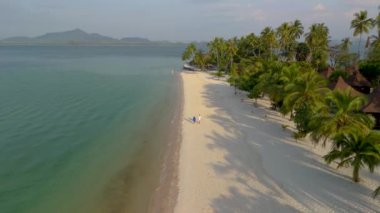 Birkaç erkek ve kadın Koh Muk plajında yürüyor. Palmiye ağaçları, yumuşak beyaz kum ve Koh Mook Trang Tayland 'da turkuaz renkli bir okyanus.