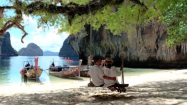 Koh Hong Adası Krabi Tayland, Koh Hong plajında salıncakta sallanan birkaç erkek ve kadın, Asyalı kadınlar ve Avrupalı erkeklerin olduğu beyaz bir plaj.