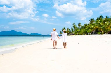 Yazlık şapkalı bir çift Koh Muk plajında yürüyorlar. Palmiye ağaçları, yumuşak beyaz kum ve Koh Mook Trang Tayland 'da turkuaz renkli bir okyanus.