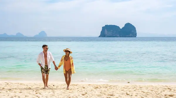 Happy young couple, an Asian woman and European men on the beach of Koh Ngai island, soft white sand, and a turqouse colored ocean in Koh Ngai Trang Thailand